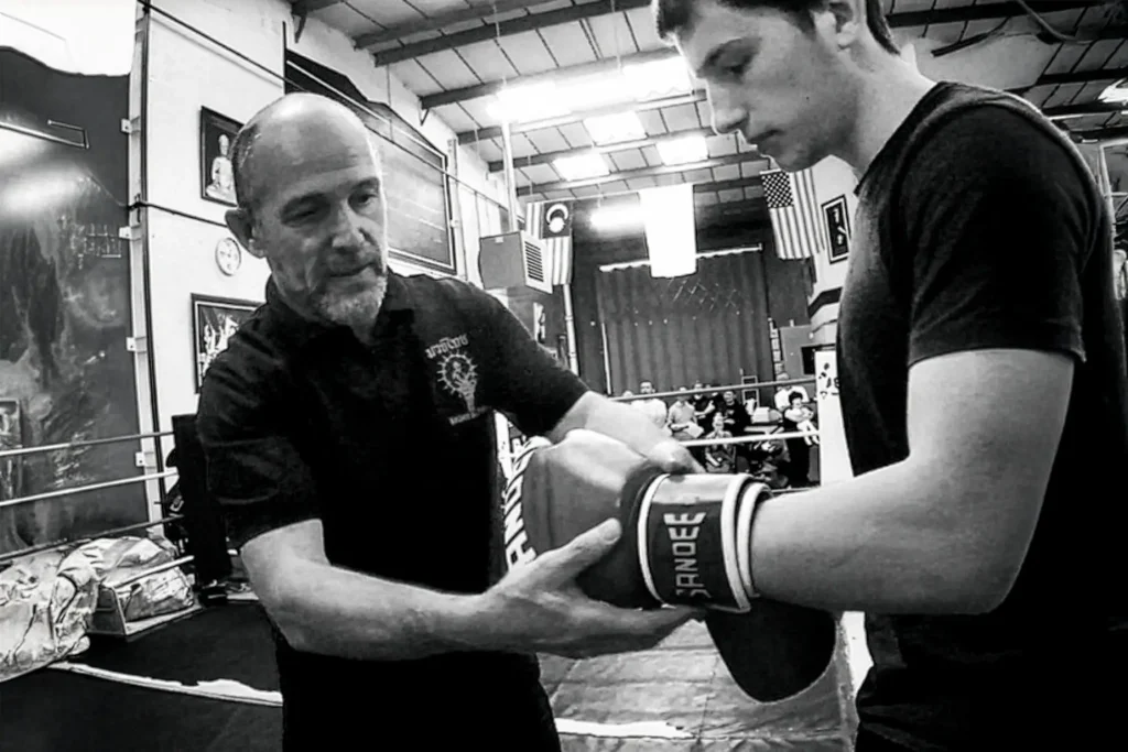 Instructor de Muay Thai guiando a un estudiante durante el ajuste de guantes de boxeo en un gimnasio de entrenamiento. Instructor de Muay Thai guiando a un estudiante durante el ajuste de guantes de boxeo en un gimnasio de entrenamiento.