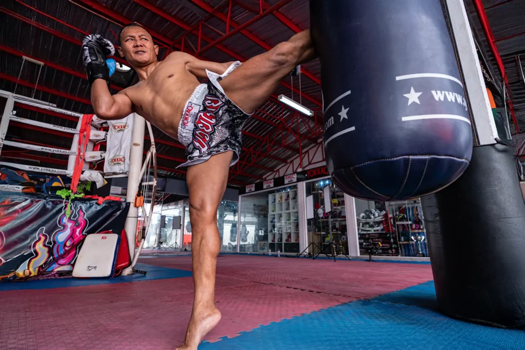 Boxeador de Muay Thai realizando una patada alta en un saco pesado en un gimnasio de entrenamiento